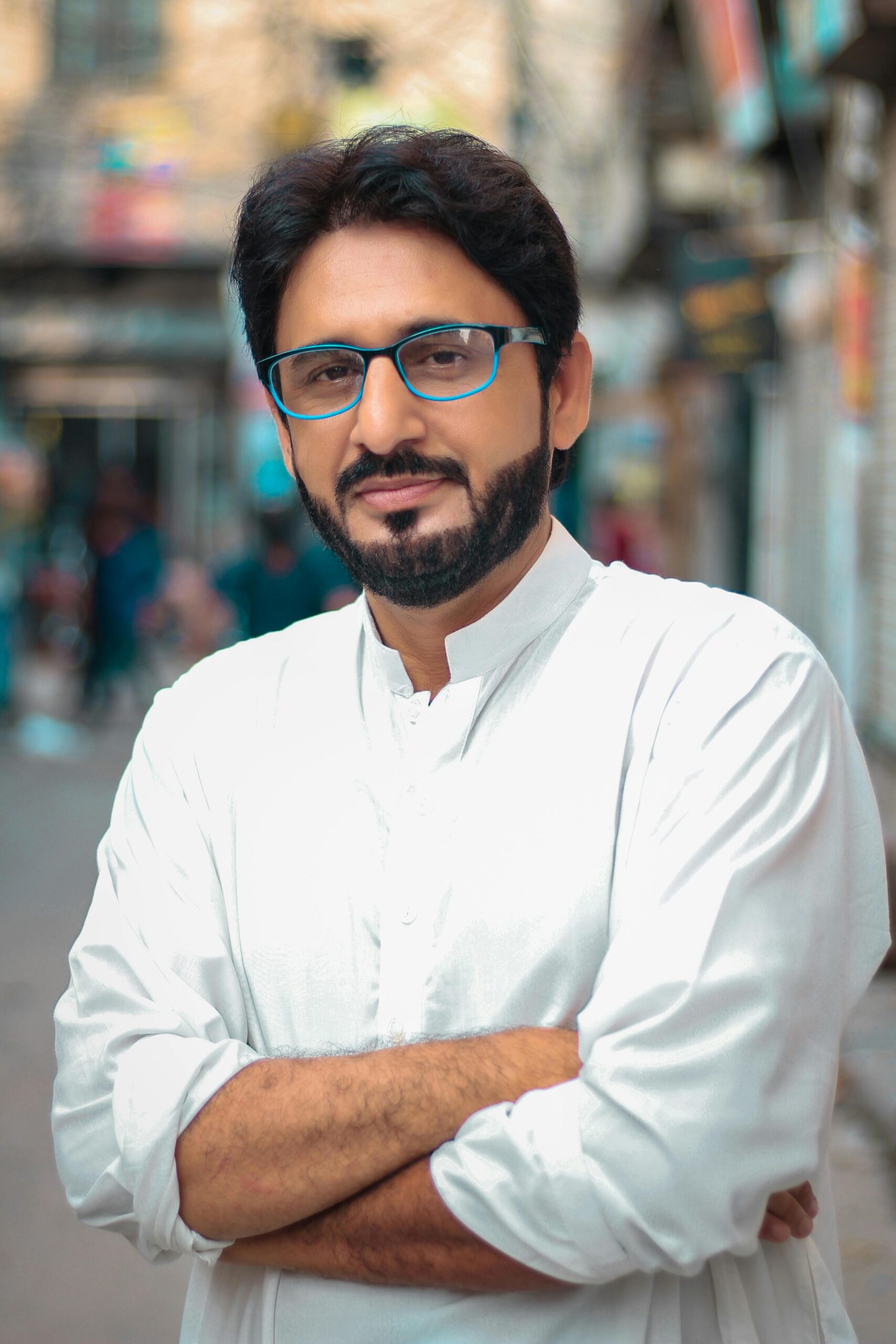 Portrait of a confident man with glasses in a city setting, wearing white attire.